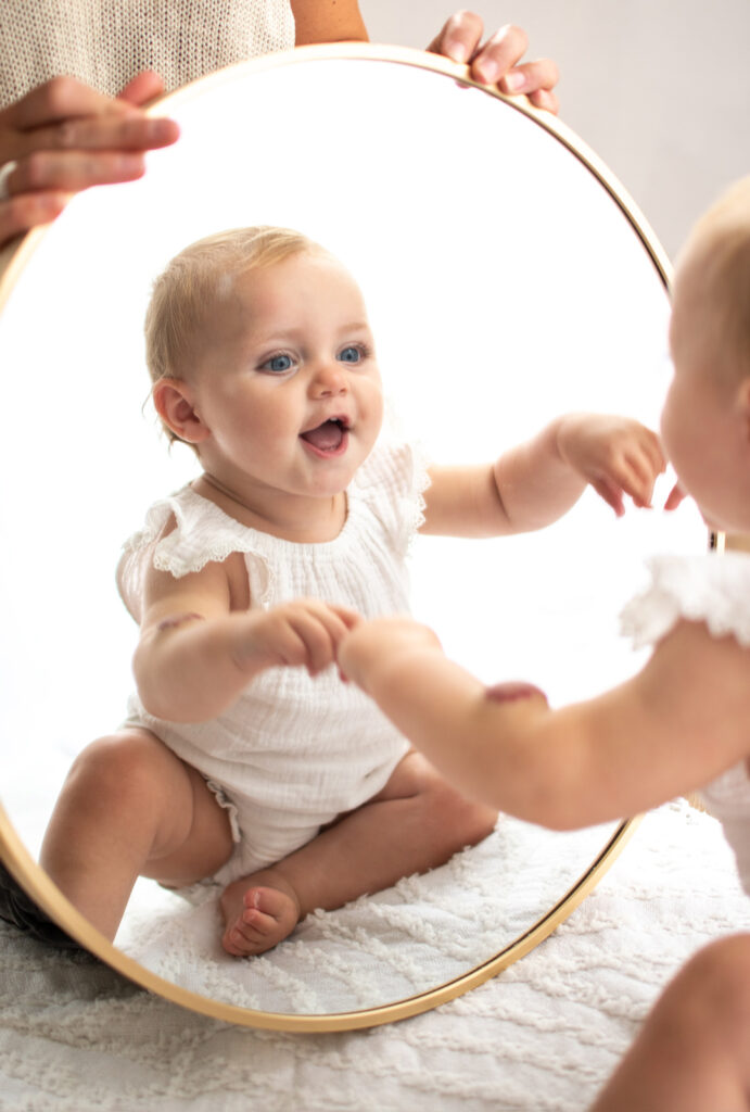 Baby girl, looking at her reflection in a mirror during. s lifestyle shoot, by Elizabeth Cole Photography who offers Family Photography in West Sussex or Surrey